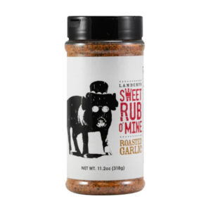 Bottle of Sweet Rub O’ Mine Roasted Garlic Rub beside grilled steak and ribs