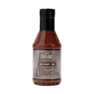 Bottle of Texas Oil Dust Brandin’ Oil BBQ Sauce beside glazed brisket and ribs