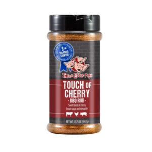 Bottle of Three Little Pigs Touch of Cherry BBQ Rub beside glazed ribs and chicken