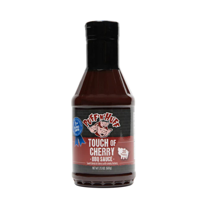 Bottle of Three Little Pigs Touch of Cherry BBQ Sauce beside glazed ribs and pork