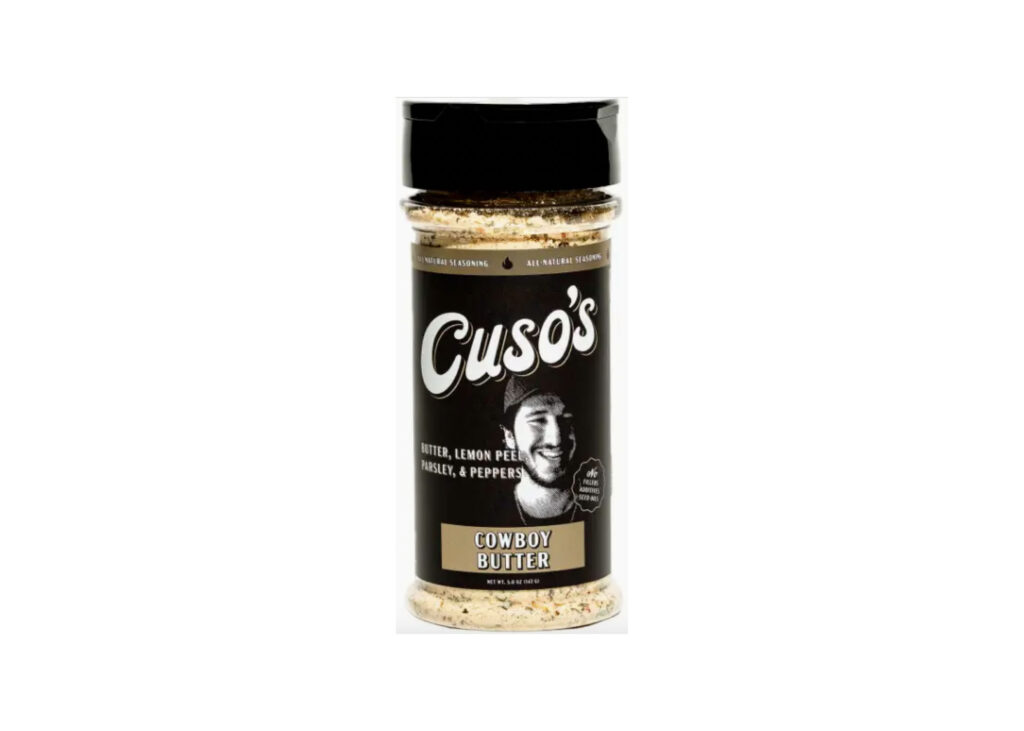 Bottle of Cuso Cuts Cowboy Butter Seasoning beside grilled steak with melted butter and lemon wedges
