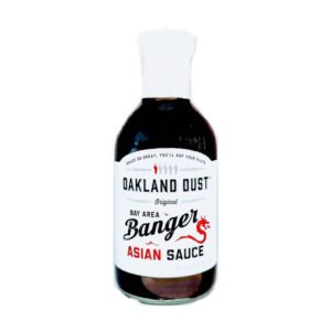 Bottle of Oakland Dust Bay Area Banger Asian Sauce beside grilled chicken skewers with sauce glaze