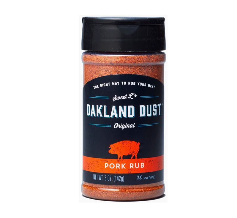 Shaker bottle of Oakland Dust Pork Rub beside grilled pork chops with golden caramel crust