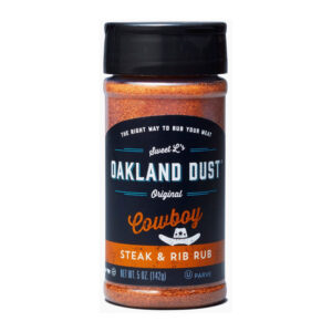 Shaker bottle of Oakland Dust Cowboy Steak & Rib Rub beside grilled rib-eye steak with peppery crust