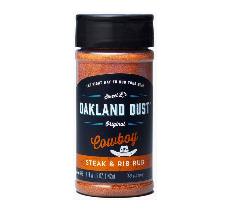 Shaker bottle of Oakland Dust Cowboy Steak & Rib Rub beside grilled rib-eye steak with peppery crust