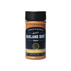 Shaker bottle of Oakland Dust Hickory Garlic Rub next to grilled pork chops with golden crust