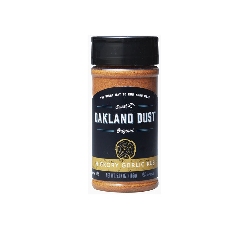 Shaker bottle of Oakland Dust Hickory Garlic Rub next to grilled pork chops with golden crust