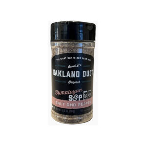 Shaker bottle of Oakland Dust Pink Himalayan Salt & Pepper beside a grilled ribeye steak with a light dusting