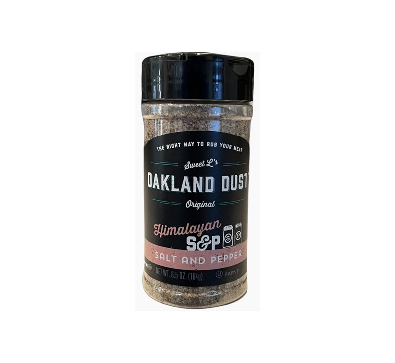 Shaker bottle of Oakland Dust Pink Himalayan Salt & Pepper beside a grilled ribeye steak with a light dusting