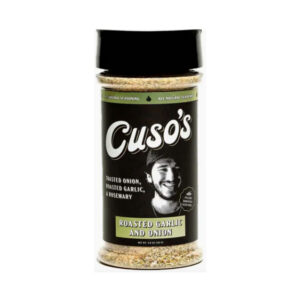 Bottle of Cuso’s Roasted Garlic & Onion Seasoning beside grilled steak and roasted garlic cloves on a wooden board