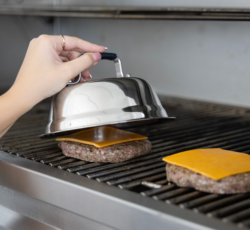 Hand placing stainless cheese melting dome over burger