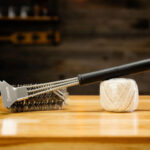 Stainless steel grill brush resting on wooden surface